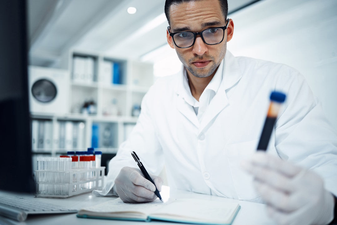 CRP-Test: Mann im Laborkittel hält Röhrchen mit Blut und macht sich Notizen