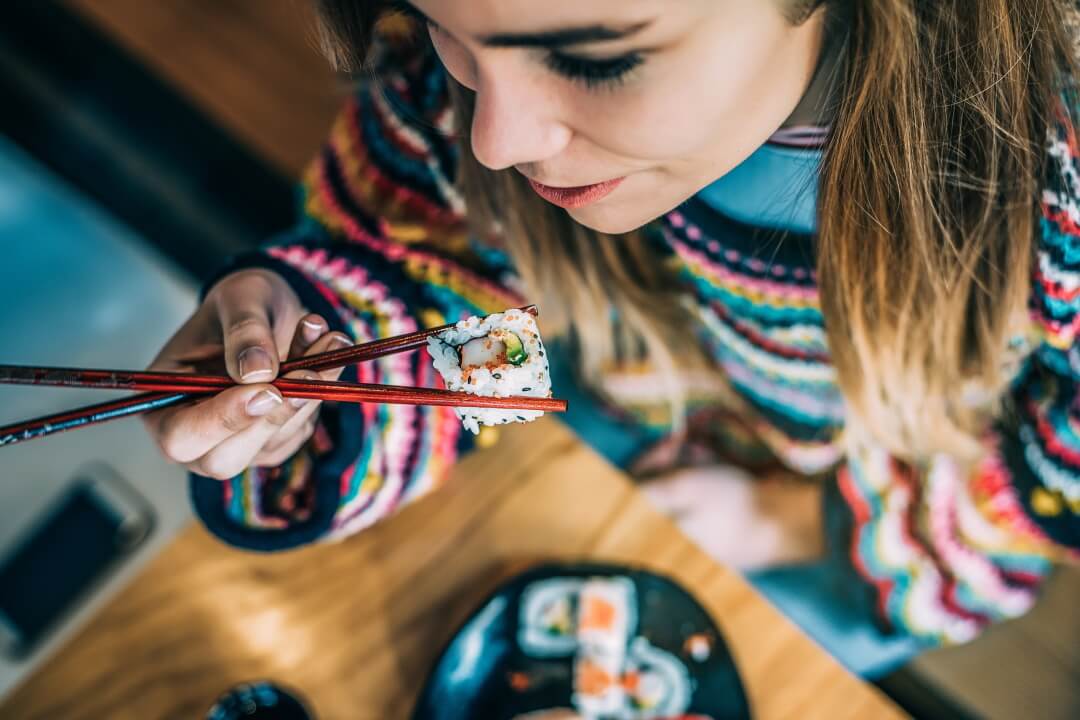 Frau isst Sushi mit Stäbchen
