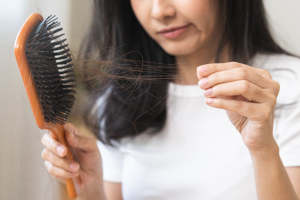 Dunkelhaarige Frau zieht viele Haare aus ihrer Bürste; Symbolbild für Haarausfall durch Zinkmangel