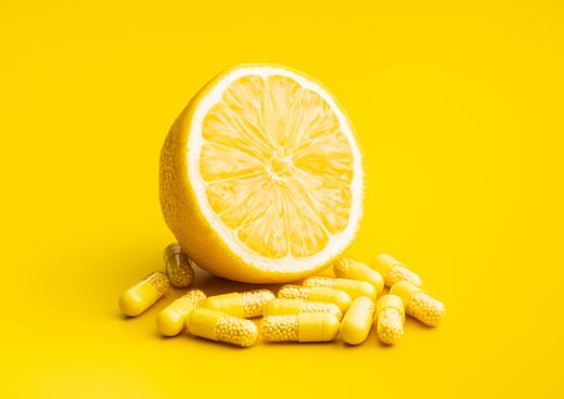 Vitamine: Zitrone und Vitaminpillen vor gelbem Hintergrund