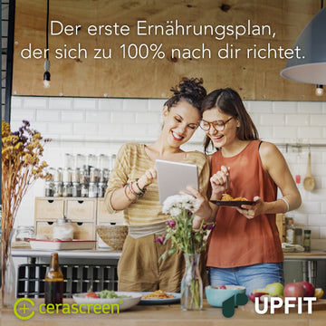 Zwei fröhliche Frauen stehen in der Küche und schauen gemeinsam auf ein Tablet